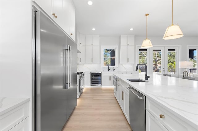 kitchen featuring sink, high quality appliances, light stone counters, white cabinetry, and wine cooler