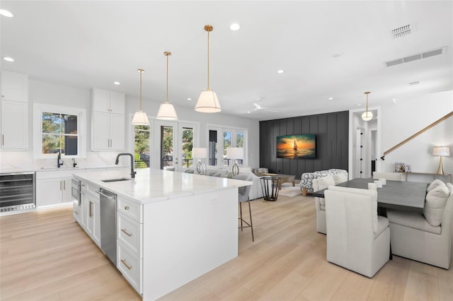 kitchen featuring a healthy amount of sunlight, an island with sink, white cabinets, and beverage cooler