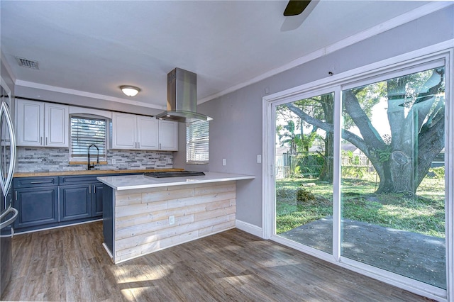 kitchen featuring island exhaust hood, ornamental molding, dark hardwood / wood-style floors, decorative backsplash, and kitchen peninsula