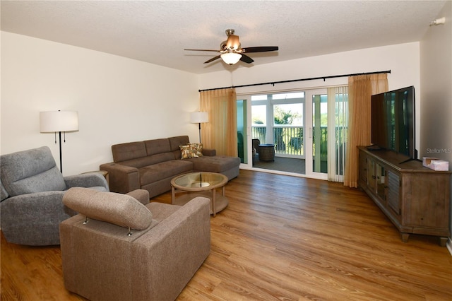 living room with a textured ceiling, light wood-type flooring, and ceiling fan