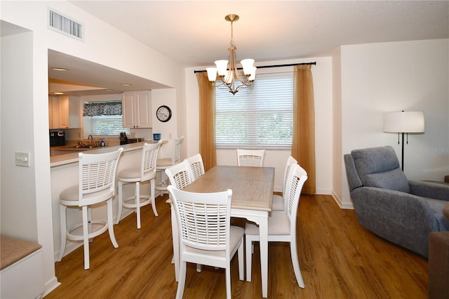 dining space with a wealth of natural light, hardwood / wood-style flooring, and an inviting chandelier