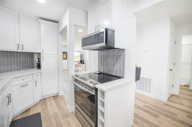 kitchen with appliances with stainless steel finishes, white cabinetry, backsplash, and light hardwood / wood-style floors