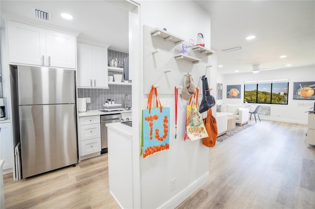 kitchen with appliances with stainless steel finishes, white cabinetry, tasteful backsplash, and light wood-type flooring