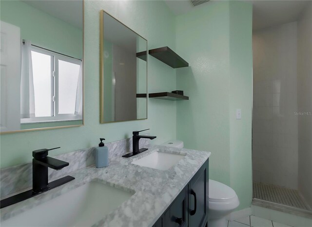 bathroom with tile patterned flooring, a tile shower, vanity, and toilet