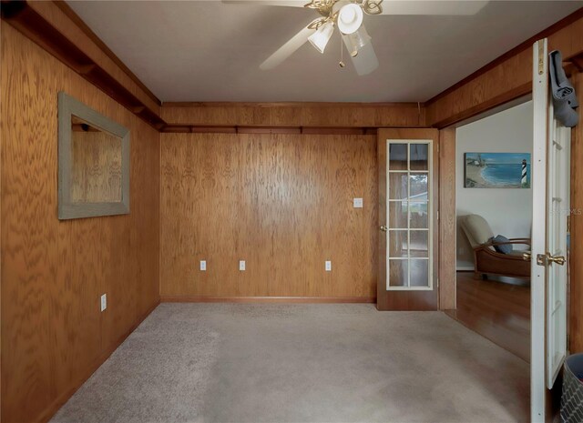 carpeted spare room featuring wood walls, crown molding, and ceiling fan