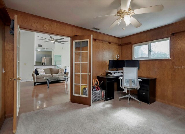 office featuring light carpet, french doors, ceiling fan, and wood walls