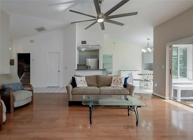 living room with high vaulted ceiling, light hardwood / wood-style floors, and ceiling fan with notable chandelier