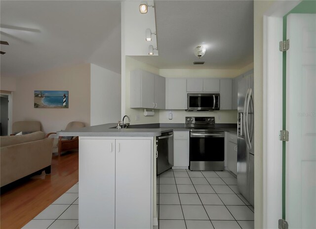 kitchen featuring kitchen peninsula, appliances with stainless steel finishes, light hardwood / wood-style flooring, white cabinets, and lofted ceiling