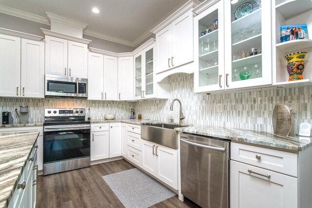 kitchen with appliances with stainless steel finishes, white cabinetry, dark wood-type flooring, crown molding, and light stone counters