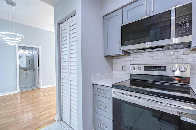 kitchen with decorative backsplash, gray cabinets, light hardwood / wood-style floors, a notable chandelier, and stainless steel appliances