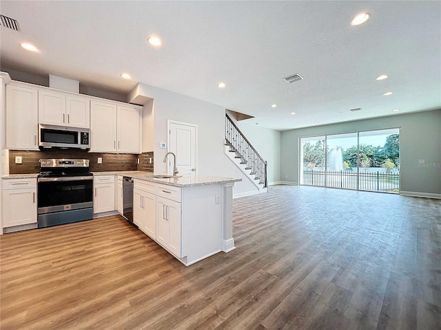 kitchen featuring white cabinets, light hardwood / wood-style floors, kitchen peninsula, and appliances with stainless steel finishes