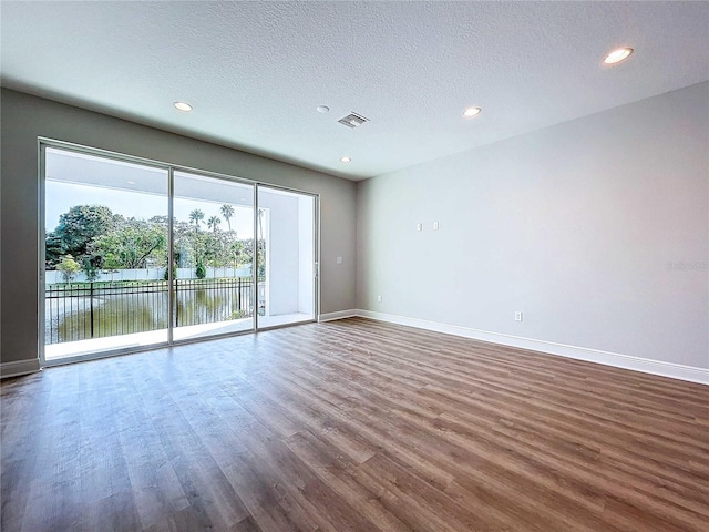 spare room with hardwood / wood-style floors, a water view, and a textured ceiling