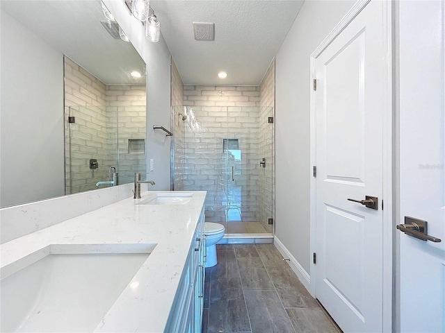 bathroom featuring a textured ceiling, vanity, toilet, and a shower with shower door