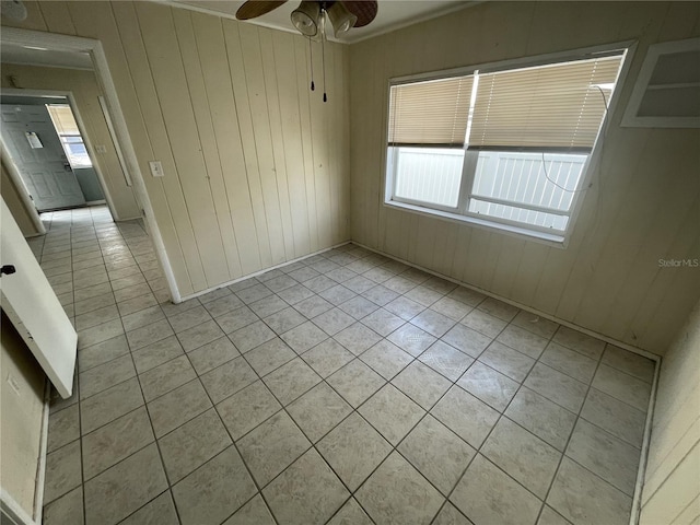 spare room featuring ceiling fan, a healthy amount of sunlight, light tile patterned floors, and wooden walls