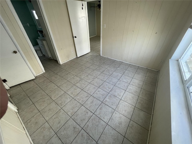 tiled empty room with ceiling fan and wood walls