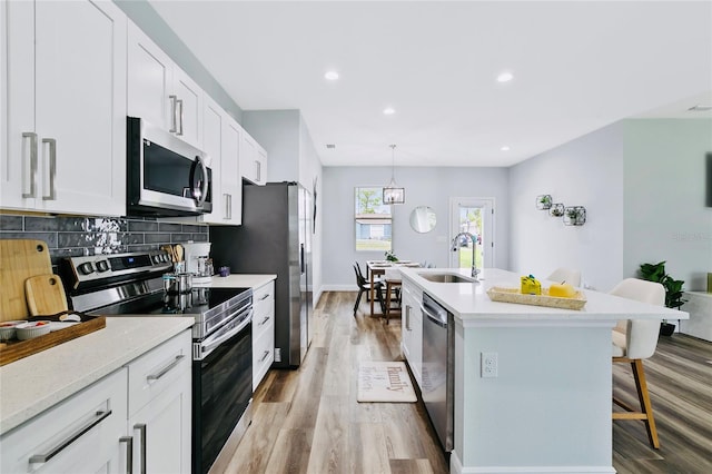 kitchen featuring white cabinets, appliances with stainless steel finishes, hanging light fixtures, and a breakfast bar area