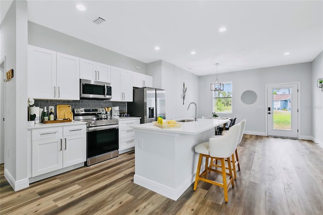 kitchen with pendant lighting, a center island with sink, white cabinets, light hardwood / wood-style floors, and stainless steel appliances