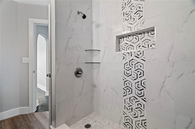 bathroom with a tile shower and wood-type flooring