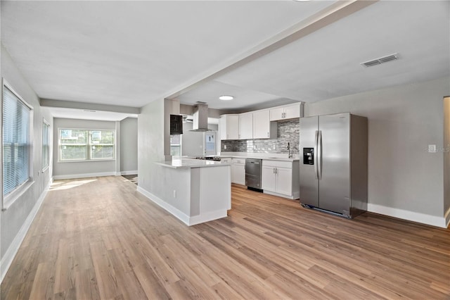 kitchen featuring tasteful backsplash, wall chimney range hood, light wood-type flooring, stainless steel appliances, and white cabinets