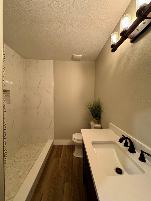 bathroom featuring tiled shower, toilet, wood-type flooring, vanity, and a textured ceiling