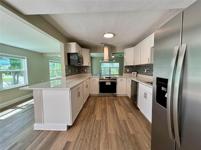 kitchen with island range hood, kitchen peninsula, stainless steel appliances, white cabinets, and light hardwood / wood-style flooring