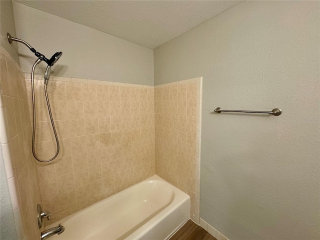 bathroom with a textured ceiling, wood-type flooring, and tiled shower / bath