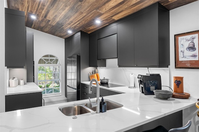 kitchen featuring cooktop, sink, kitchen peninsula, stainless steel fridge, and light stone counters