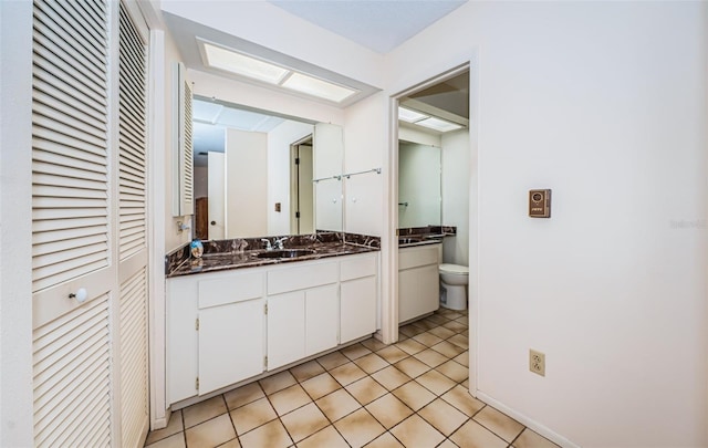 bathroom with a closet, toilet, vanity, and tile patterned flooring