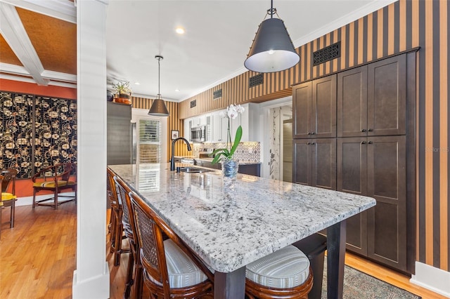 kitchen with crown molding, a center island with sink, hanging light fixtures, and light wood-type flooring