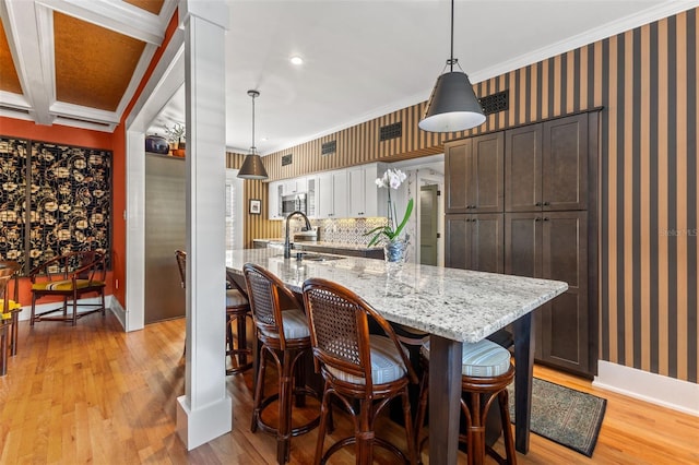 kitchen with sink, hanging light fixtures, crown molding, and light wood-type flooring