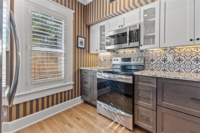 kitchen with white cabinets, tasteful backsplash, appliances with stainless steel finishes, light stone countertops, and light wood-type flooring