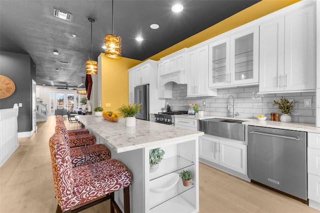 kitchen with premium appliances, sink, light wood-type flooring, white cabinetry, and decorative light fixtures