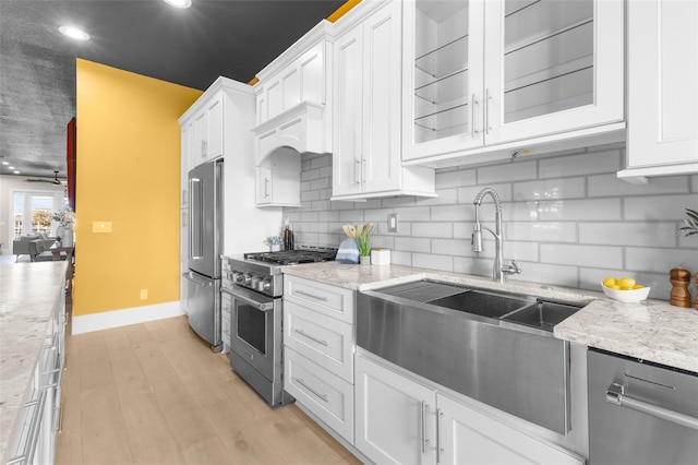 kitchen with light hardwood / wood-style flooring, stainless steel appliances, backsplash, light stone countertops, and white cabinets