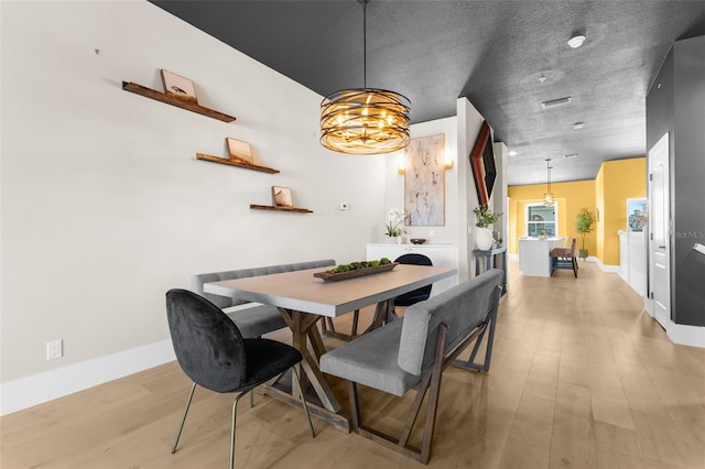 dining space featuring an inviting chandelier, a textured ceiling, and light wood-type flooring