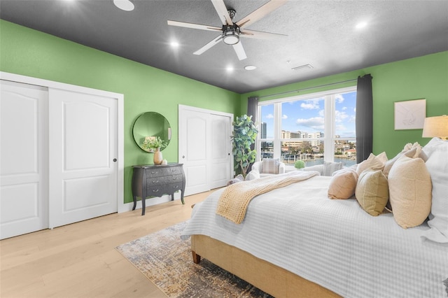 bedroom with ceiling fan, multiple closets, a textured ceiling, and light hardwood / wood-style floors