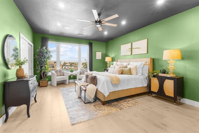 bedroom with light hardwood / wood-style flooring, a textured ceiling, and ceiling fan