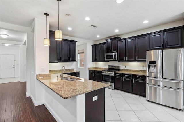 kitchen with sink, kitchen peninsula, appliances with stainless steel finishes, decorative light fixtures, and light hardwood / wood-style flooring