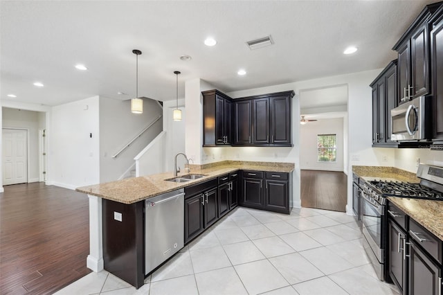 kitchen featuring sink, light stone counters, appliances with stainless steel finishes, decorative light fixtures, and light wood-type flooring