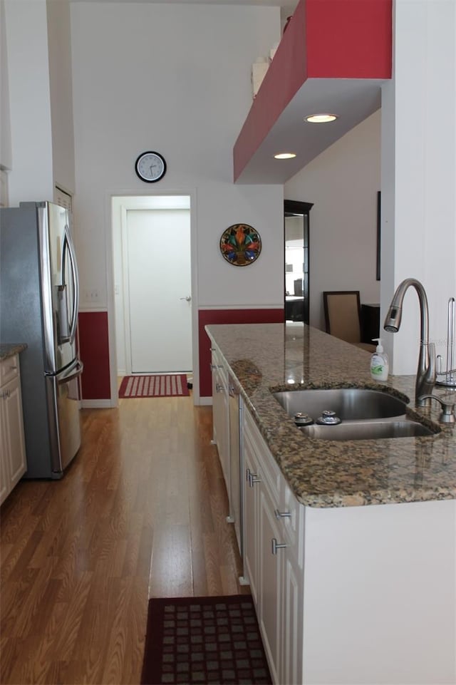 kitchen featuring stainless steel appliances, wood-type flooring, dark stone counters, sink, and white cabinets