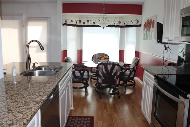 kitchen with white cabinets, hanging light fixtures, appliances with stainless steel finishes, dark hardwood / wood-style floors, and sink