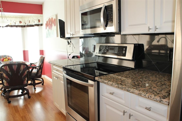 kitchen with appliances with stainless steel finishes, light hardwood / wood-style flooring, white cabinetry, and backsplash