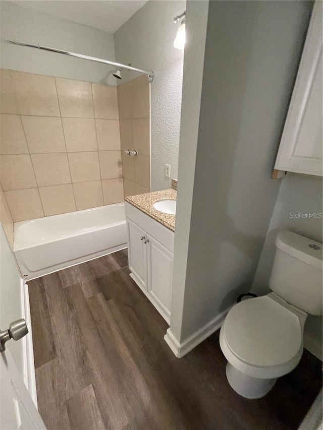 full bathroom with tiled shower / bath, vanity, wood-type flooring, and toilet