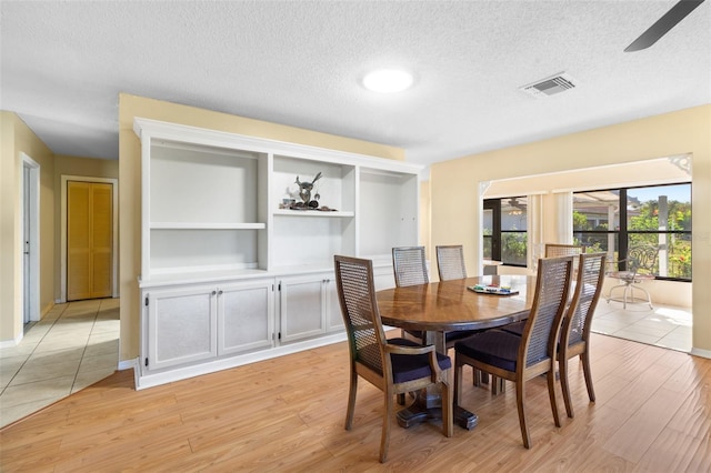 dining space with built in shelves, light wood-type flooring, a textured ceiling, and ceiling fan