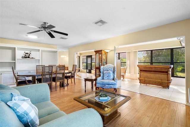 living room with built in shelves, light hardwood / wood-style flooring, a textured ceiling, and ceiling fan