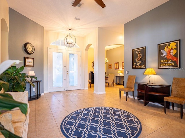 foyer entrance with french doors, ceiling fan with notable chandelier, and light tile patterned floors