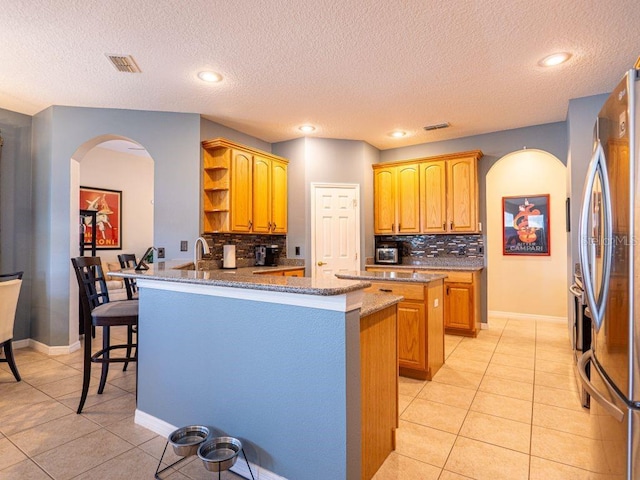 kitchen featuring kitchen peninsula, stainless steel fridge, tasteful backsplash, light tile patterned floors, and a breakfast bar area