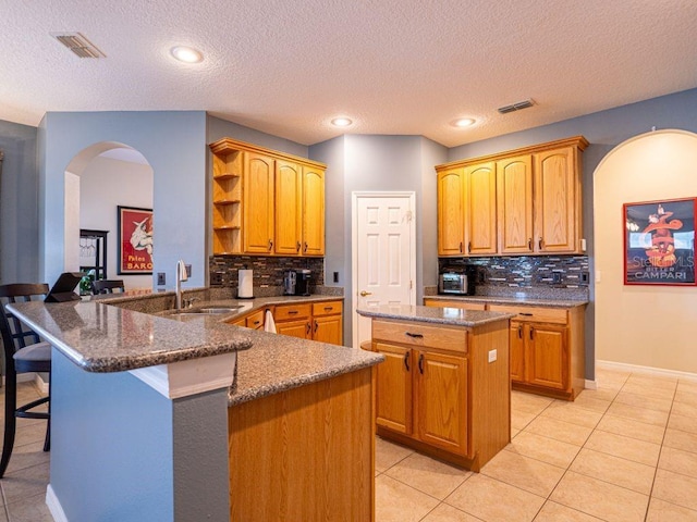 kitchen with kitchen peninsula, sink, light tile patterned floors, a center island, and a breakfast bar area