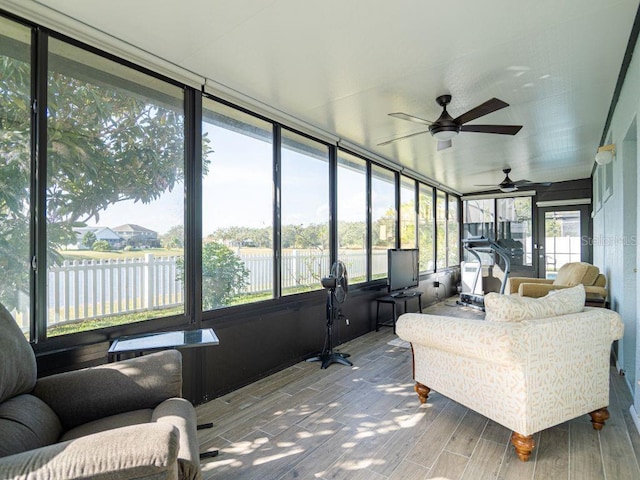 sunroom featuring ceiling fan and a water view