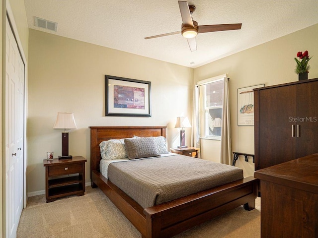 bedroom featuring ceiling fan, a closet, light carpet, and a textured ceiling