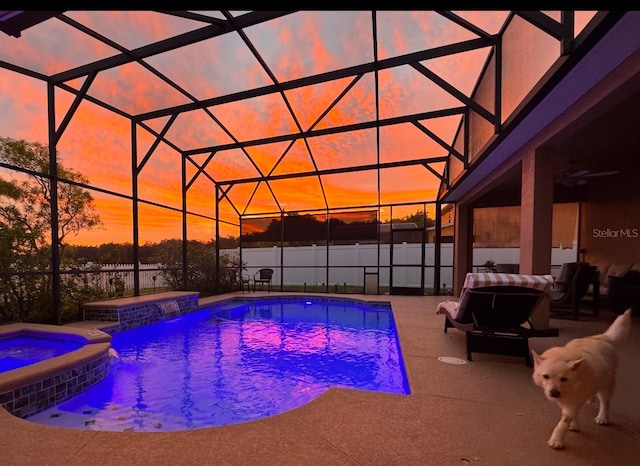 pool at dusk featuring an in ground hot tub, pool water feature, ceiling fan, glass enclosure, and a patio